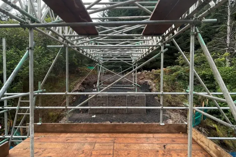 Timber-decked scaffold access structure under construction in a wooded rural setting