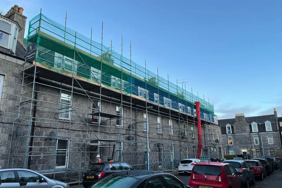 Full-length scaffold access along a granite tenement terrace in a Scottish city street, ready for re-roofing works
